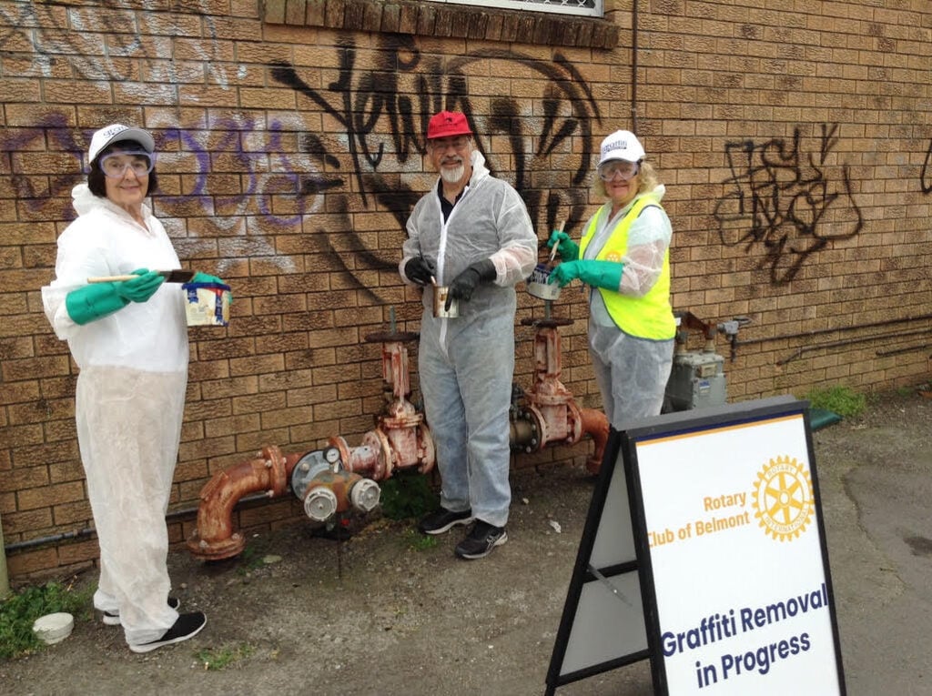 Image of three people looking at the camera in front of wall of graffiti in the process of cleaning the wall.
